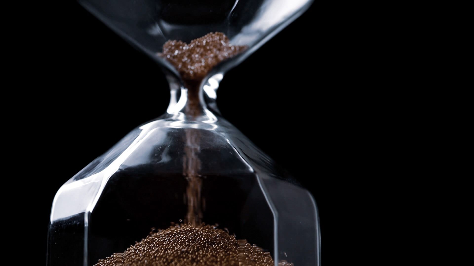 Close up of flowing sands in sandglass on a black background.