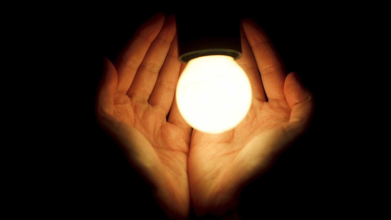 hands of human holding illuminated led bulb on black background. eco safe the planet concept. new idea or energy theme. space for text